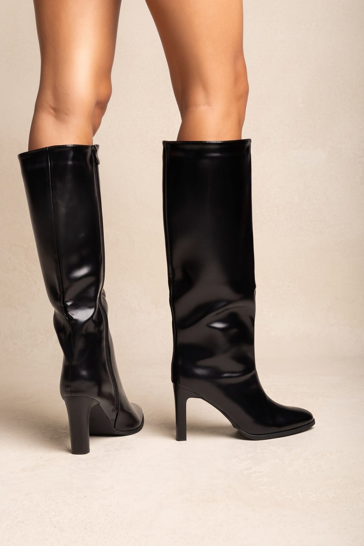 Model wearing black leather-look knee-high boots with pointed toes and block heels, legs cropped below the knee, standing in a front view
