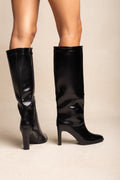 Model wearing black leather-look knee-high boots with pointed toes and block heels, legs cropped below the knee, standing in a front view