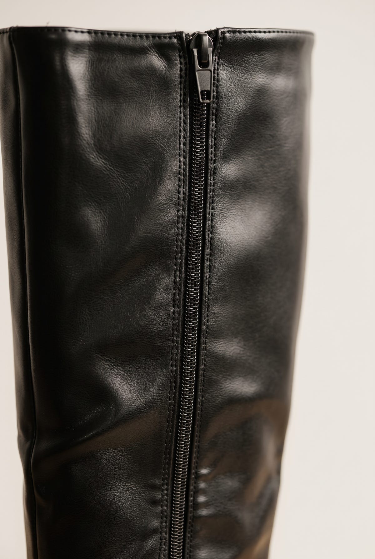Close-up of black leather-look boot shaft showing a vertical zipper running along the side seam with a soft matte texture