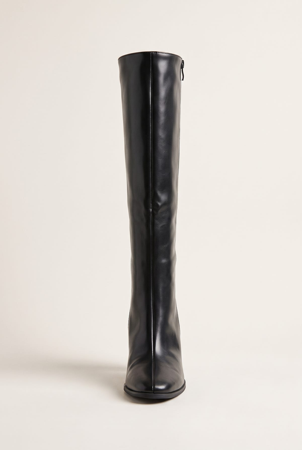 Front view of a single black knee-high boot standing upright showing the narrow shaft, pointed toe and slim heel base