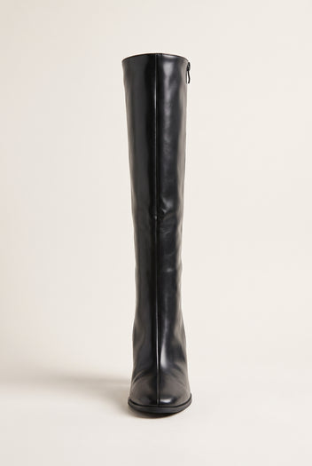 Front view of a single black knee-high boot standing upright showing the narrow shaft, pointed toe and slim heel base