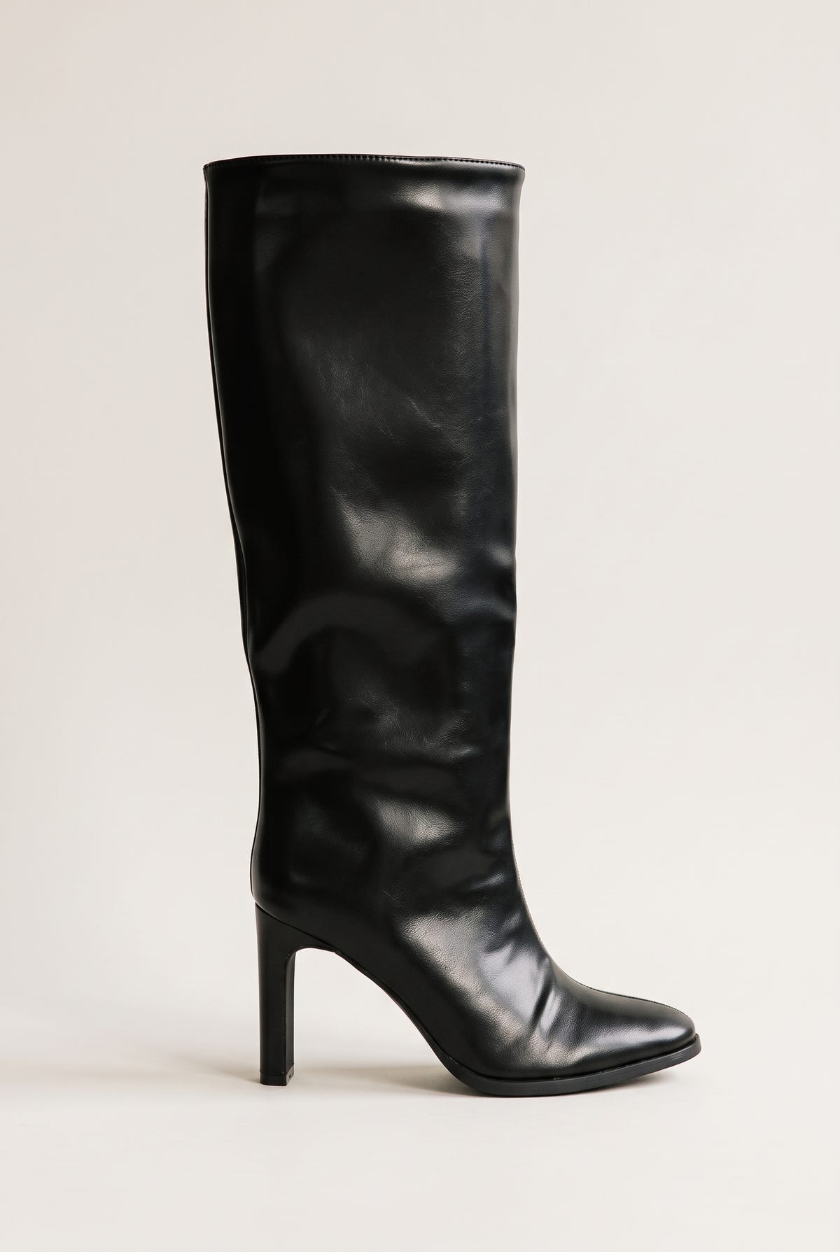 Black leather-look knee-high boot side view on a plain light surface showing the smooth tall shaft, pointed toe and tapered block heel