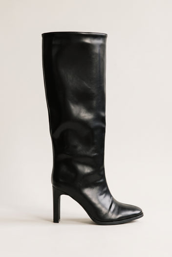 Black leather-look knee-high boot side view on a plain light surface showing the smooth tall shaft, pointed toe and tapered block heel