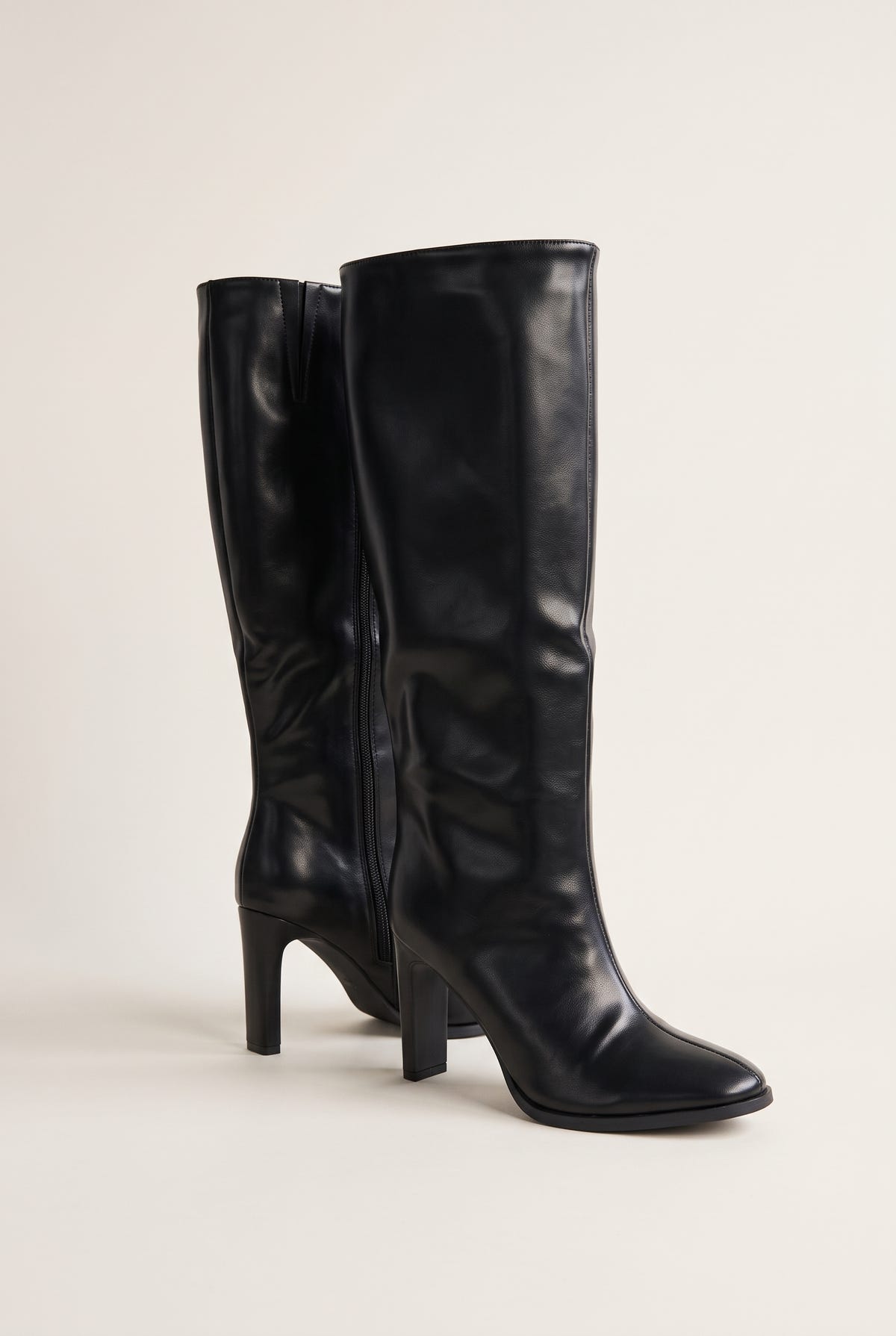 Pair of black leather-look knee-high boots in three-quarter view showing the side zipper and pointed toes with block heels