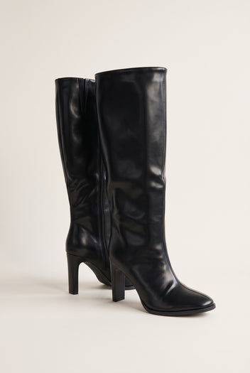 Pair of black leather-look knee-high boots in three-quarter view showing the side zipper and pointed toes with block heels