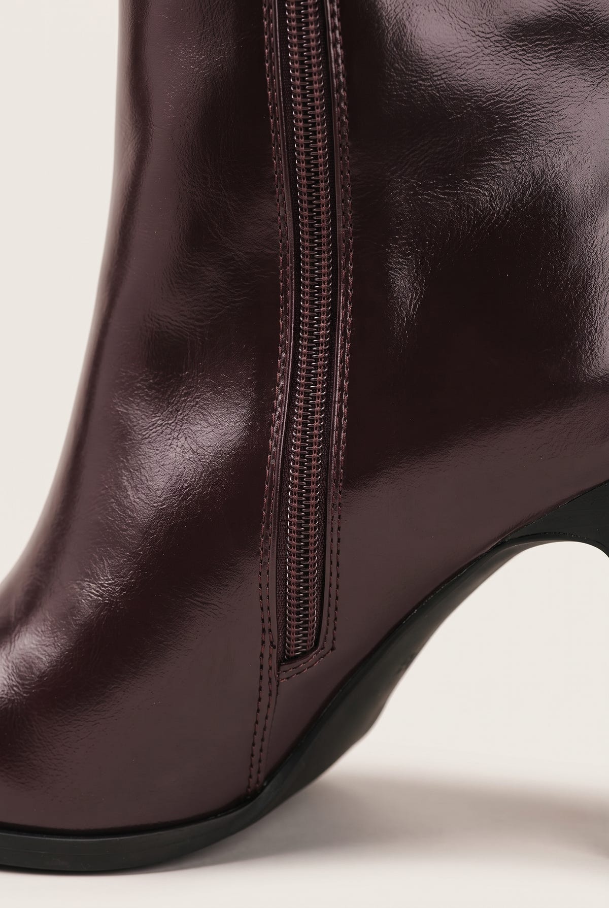 Close-up of dark brown leather boot shaft with vertical zipper and black rubber sole edge at the base
