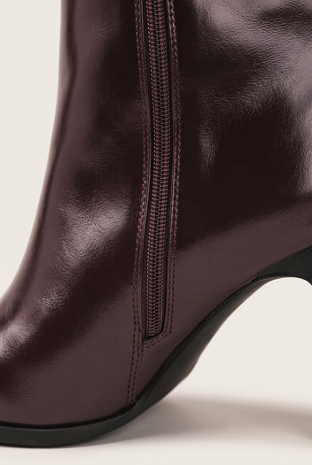 Close-up of dark brown leather boot shaft with vertical zipper and black rubber sole edge at the base