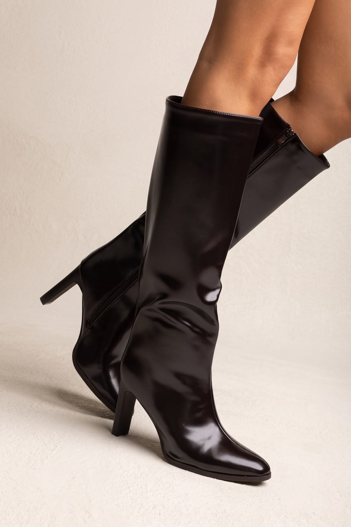 Model wearing dark brown knee-high block heel boots with one leg bent and foot lifted to show the pointed toe and heel