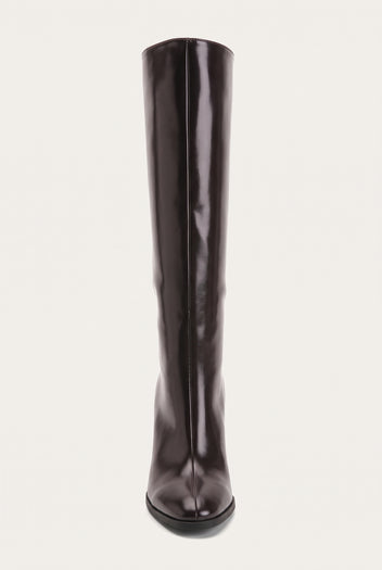 Front view of a tall dark brown boot with narrow pointed toe and smooth shaft rising straight up on a pale surface