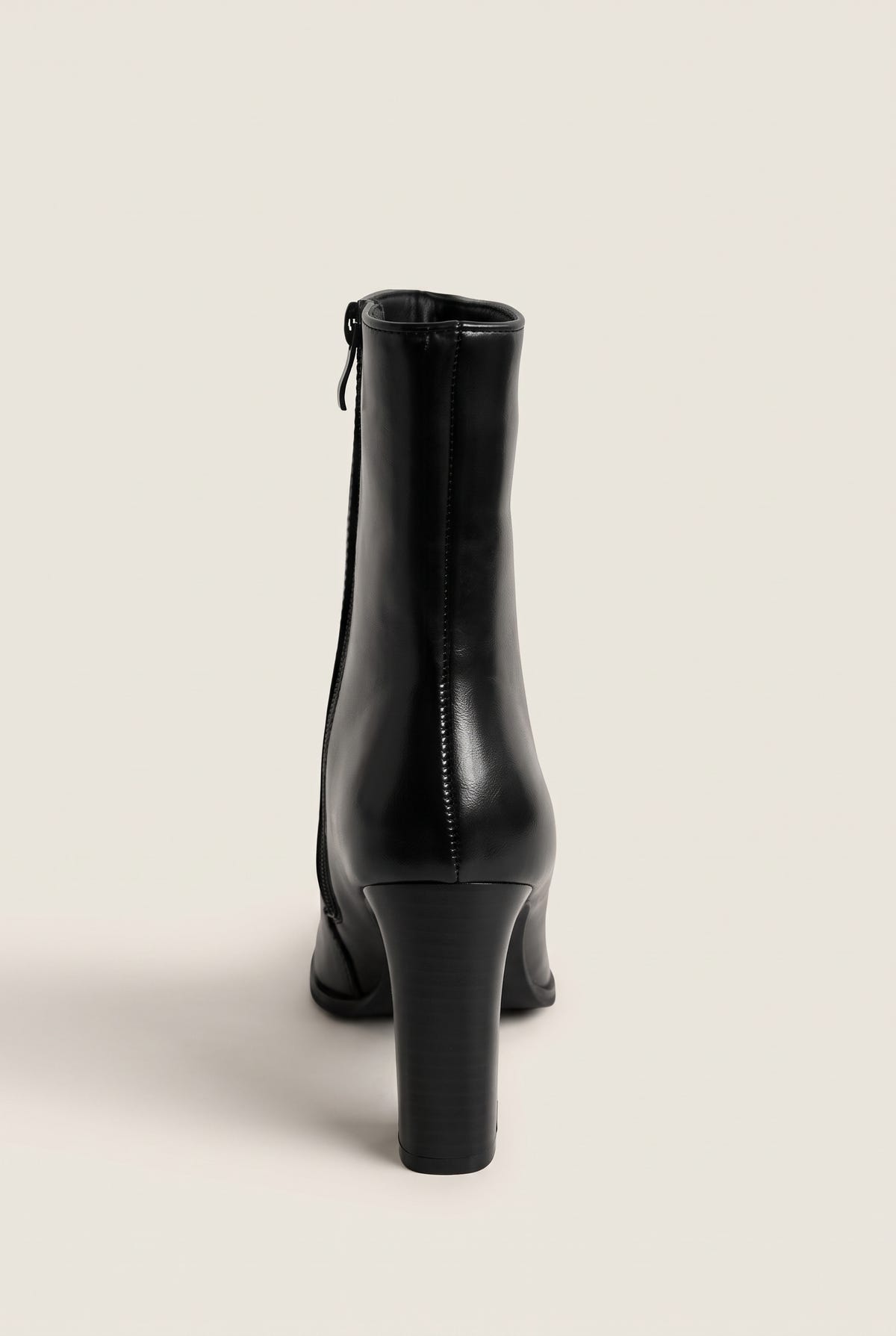 Back view of a black leather ankle boot with side zip and a tall slim block heel on white
