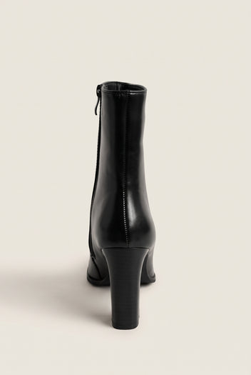 Back view of a black leather ankle boot with side zip and a tall slim block heel on white
