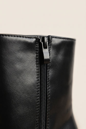 Close-up of a black leather ankle boot side zip with black zipper pull and visible stitching