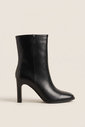 Side view of a black leather ankle boot with rounded toe and slim high block heel on white