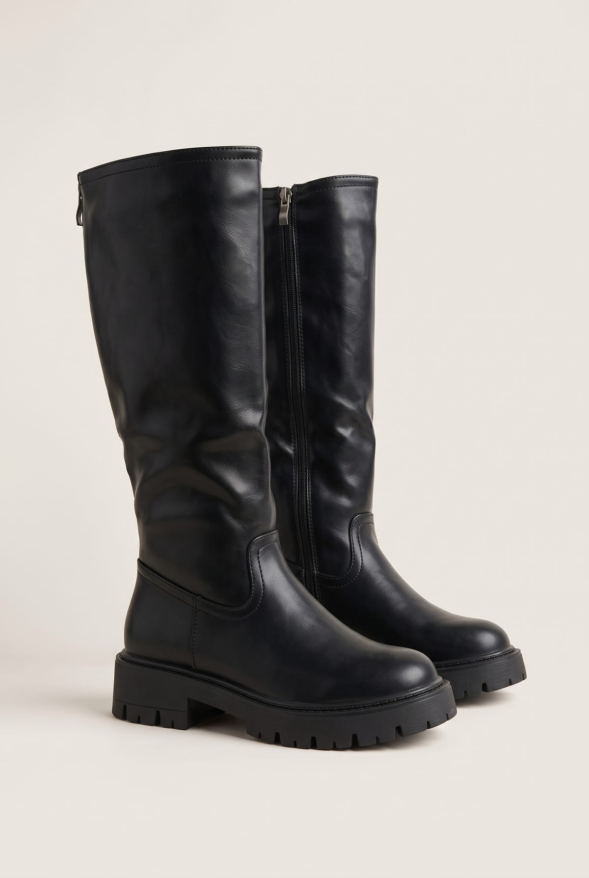 Pair of black knee-high chunky sole boots angled side by side with thick lug soles and zips on the inner shaft