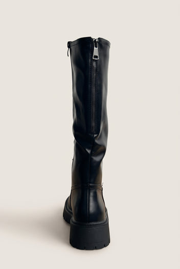 Back view of a black knee-high chunky boot showing the vertical back zipper and the thick block lug sole