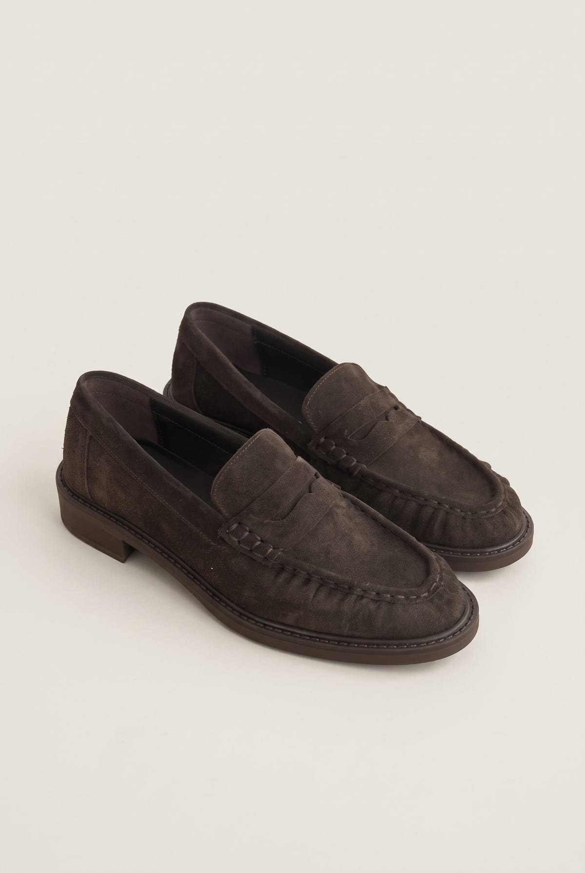 Angled pair of brown suede loafers showing flat heels, rounded toes and stitched edges