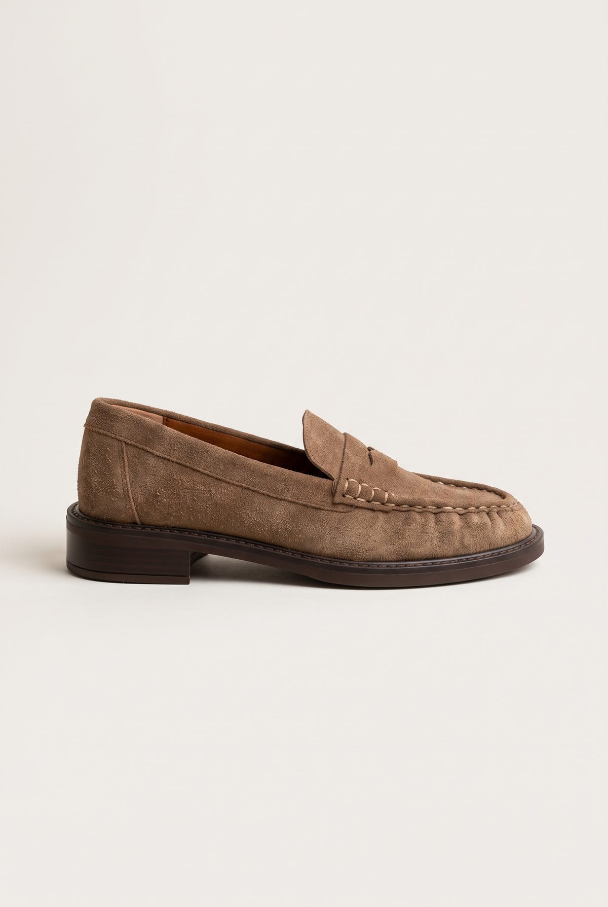 Side view of beige suede penny loafer with thin low sole, stitched moc toe and penny strap