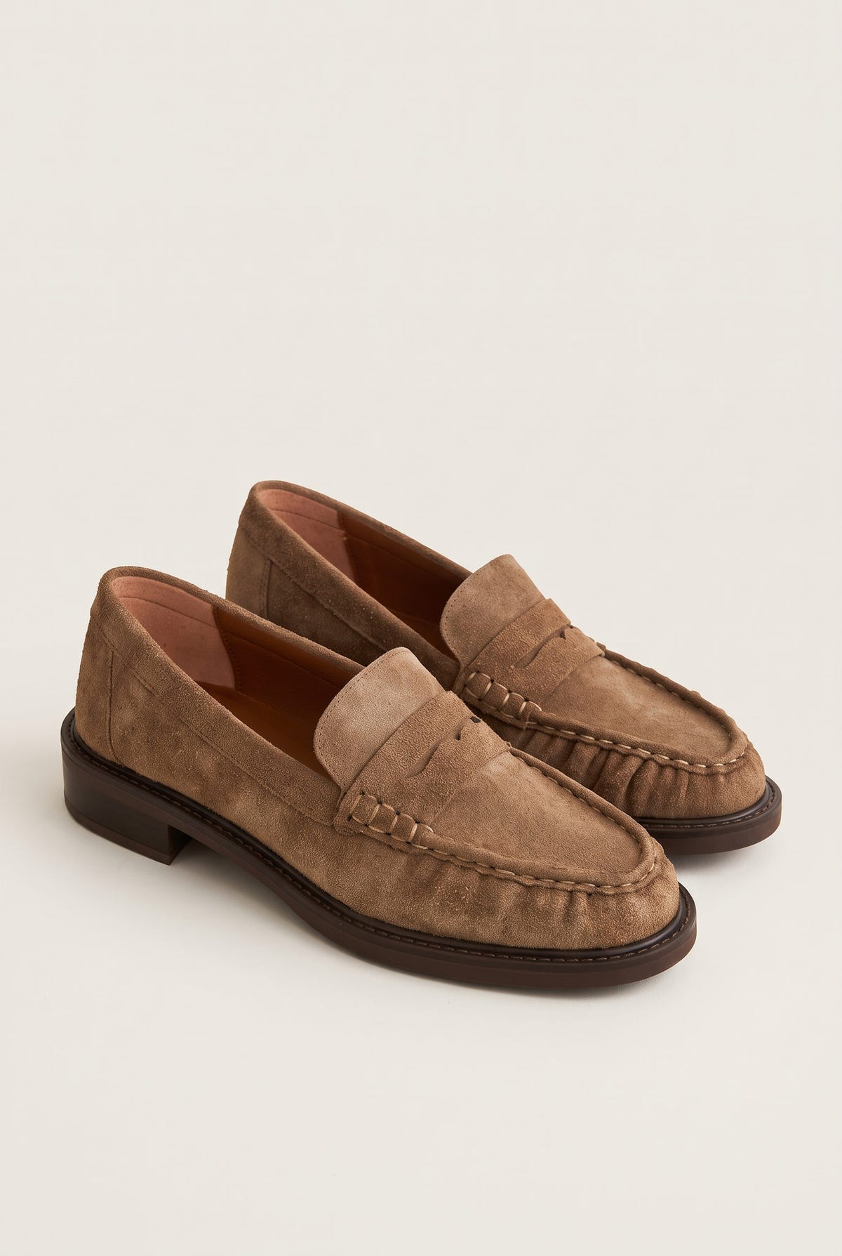 Angled pair of beige suede penny loafers with flat low heels and stitched rounded toes