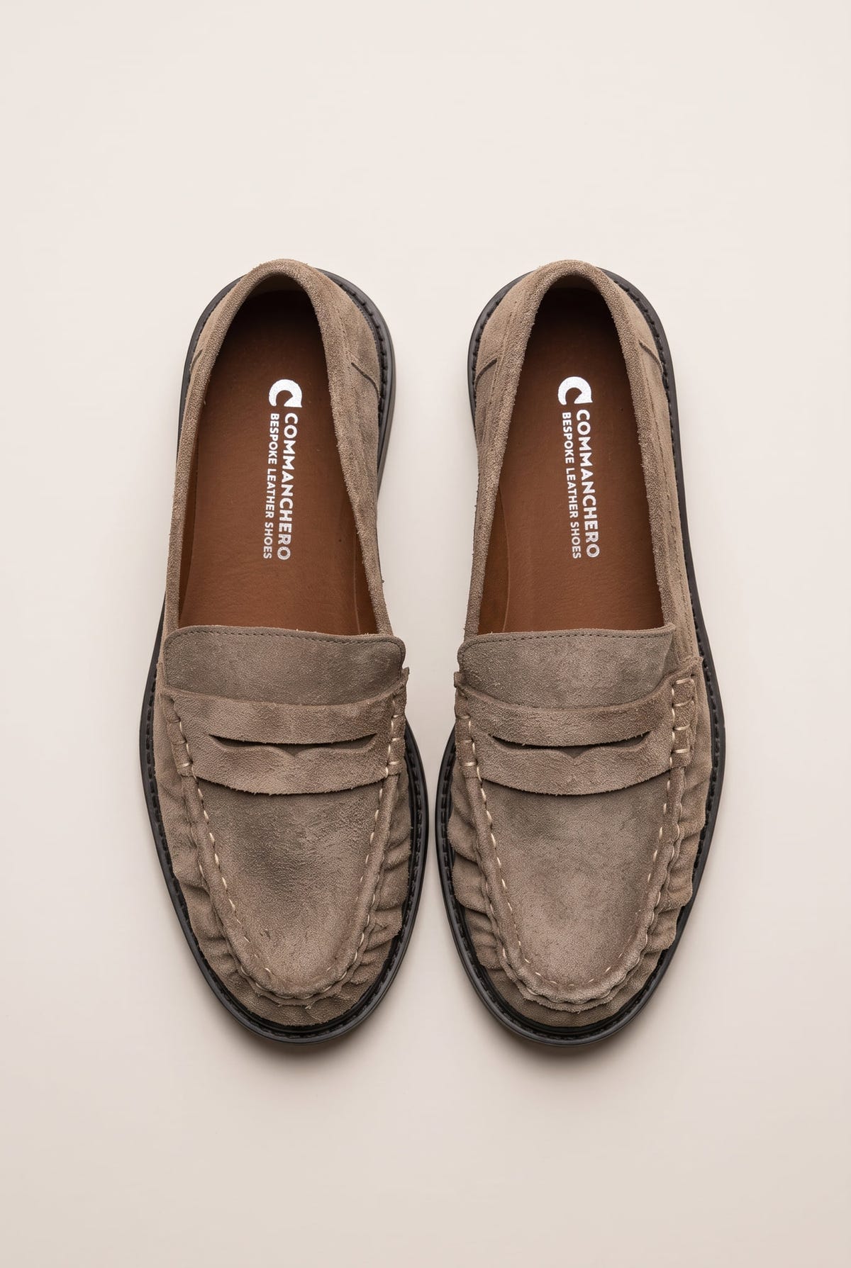 Top view of beige suede penny loafers with stitched rounded toes and cushioned tan insoles