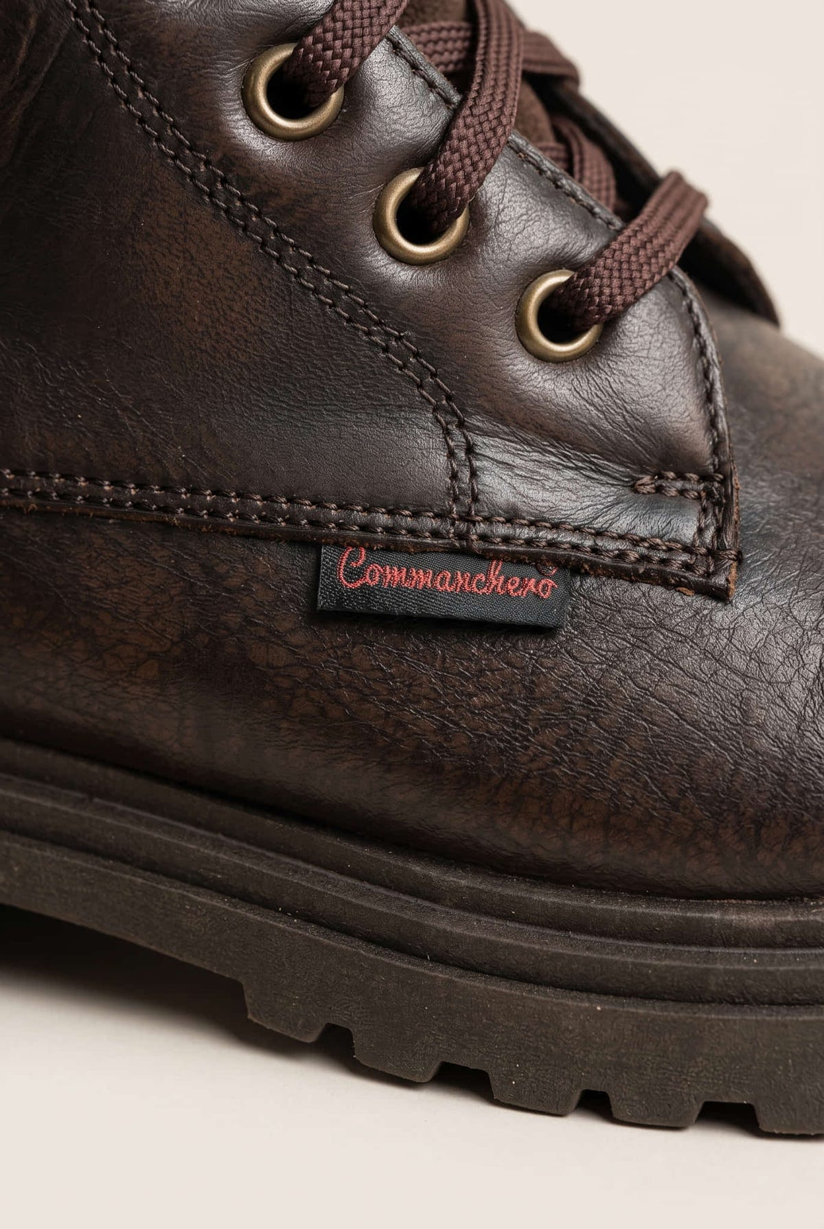 Close-up of brown matte lace-up boot with brass eyelets and stitched lugged rubber sole edge