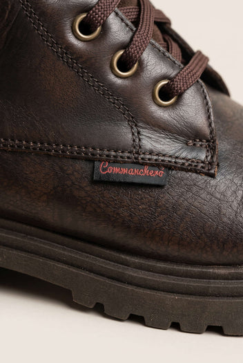 Close-up of brown matte lace-up boot with brass eyelets and stitched lugged rubber sole edge