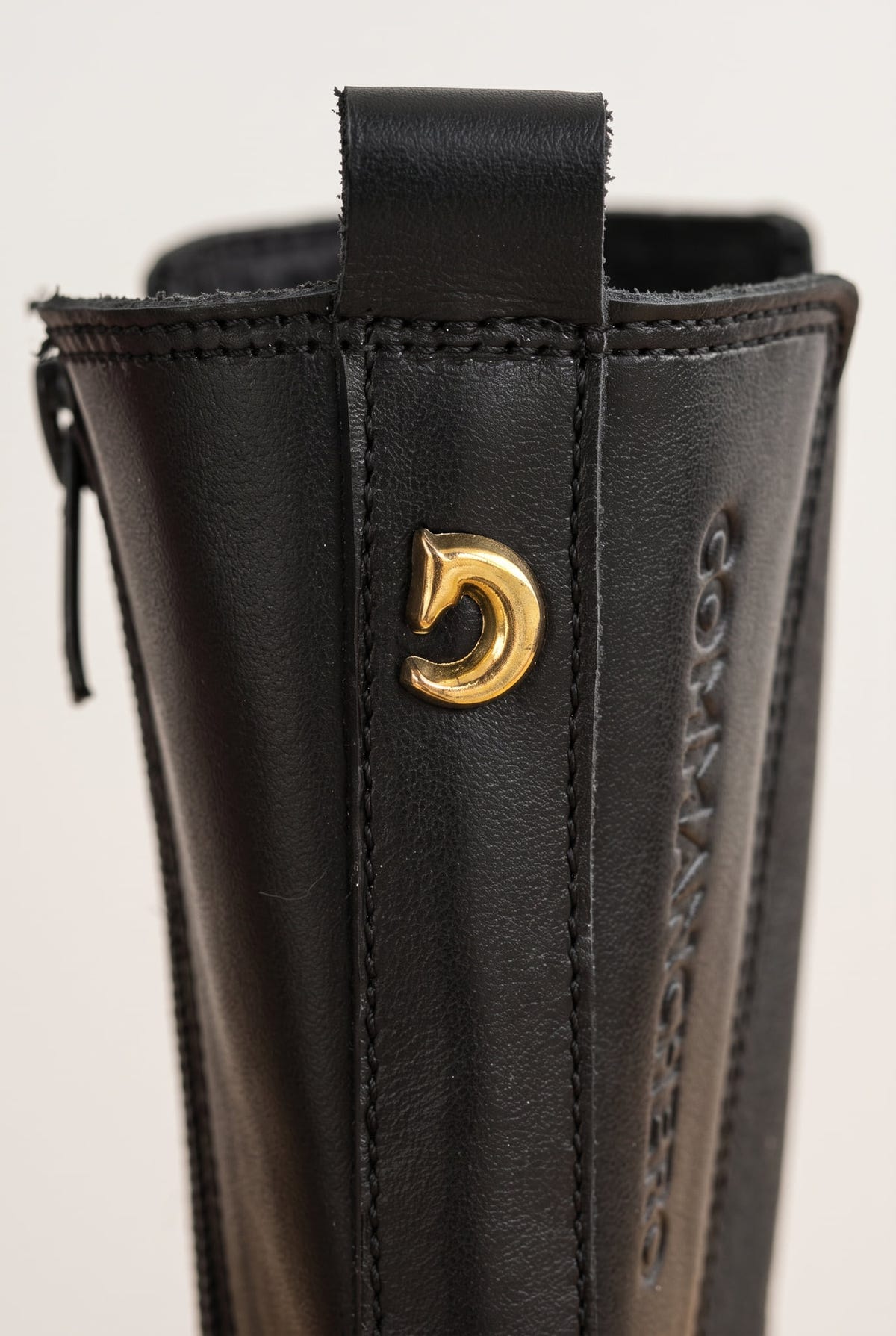 Close-up of black matte boot back with side zipper and gold-toned emblem near the pull loop