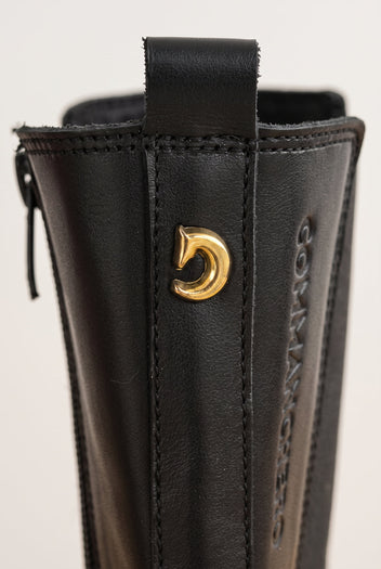 Close-up of black matte boot back with side zipper and gold-toned emblem near the pull loop