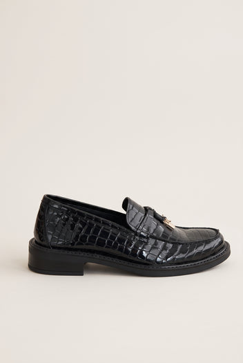 Black croc-embossed leather loafer with a metal ornament on the strap, side view showing the low sole