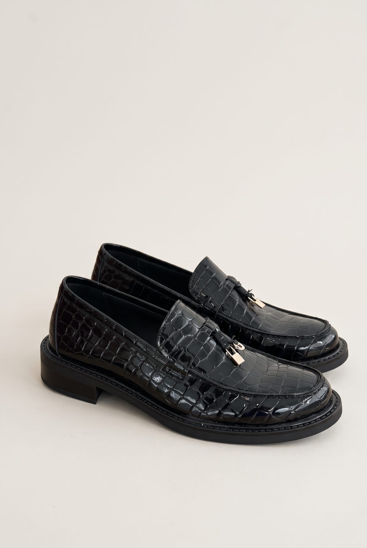 Pair of black croc-embossed loafers in three-quarter view, metal charm on the strap and low chunky soles