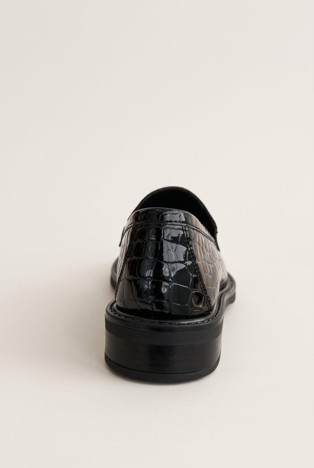 Black croc-embossed loafer seen from behind, showing the glossy heel counter and thick black sole