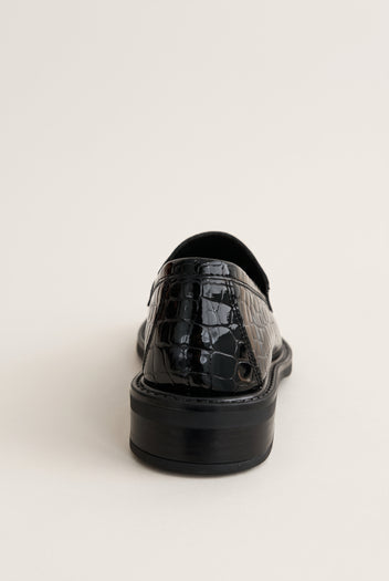 Black croc-embossed loafer seen from behind, showing the glossy heel counter and thick black sole