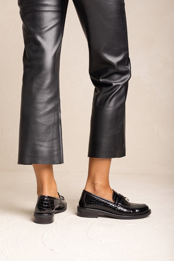 Glossy black patent loafer with metal detail on the strap, pair shown beside black leather trousers