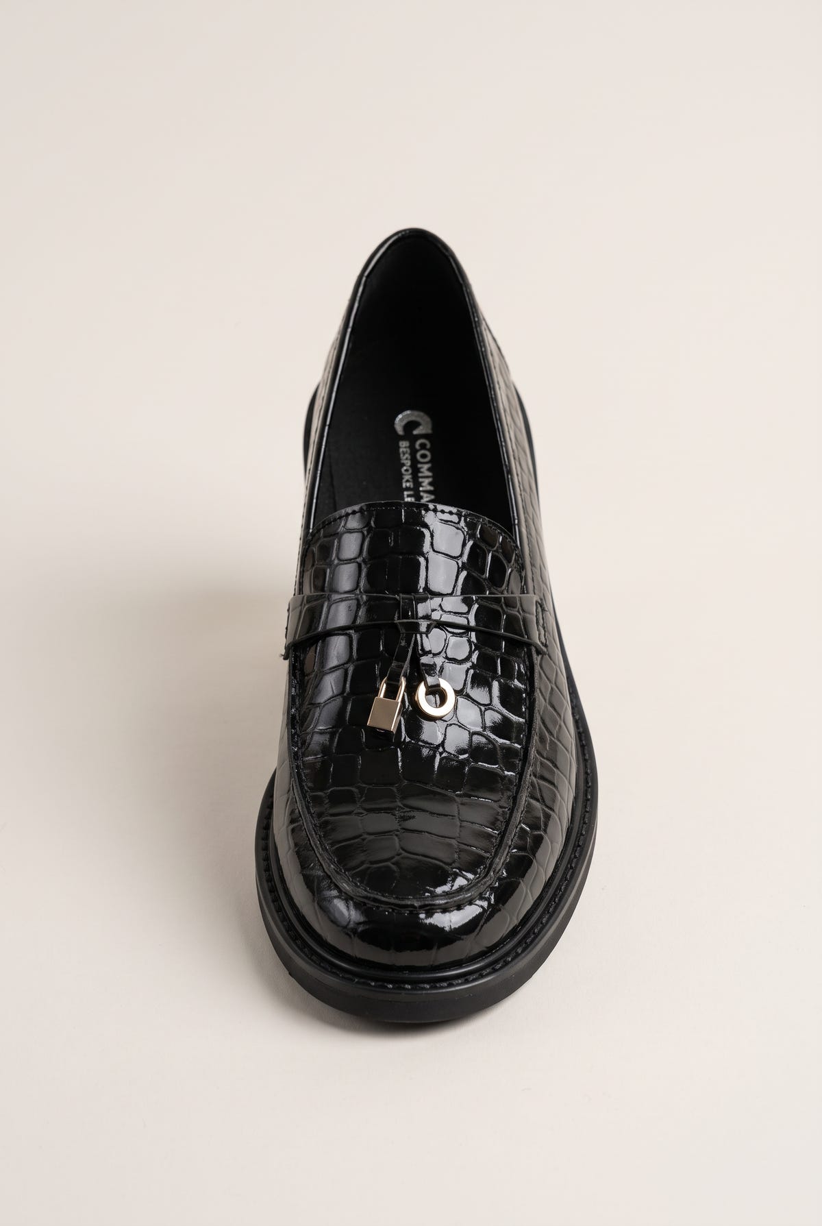 Black croc-embossed loafer seen from the front, glossy finish with a metal charm on the strap and a chunky sole