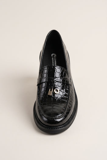 Black croc-embossed loafer seen from the front, glossy finish with a metal charm on the strap and a chunky sole