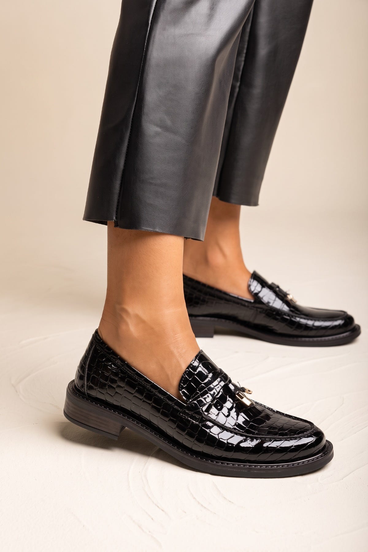 Black croc-embossed loafer with glossy finish and metal detail, side view on model legs