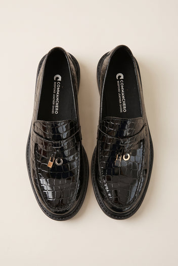 Pair of black croc-embossed glossy leather loafers seen from above, metal charm on each strap and a chunky sole