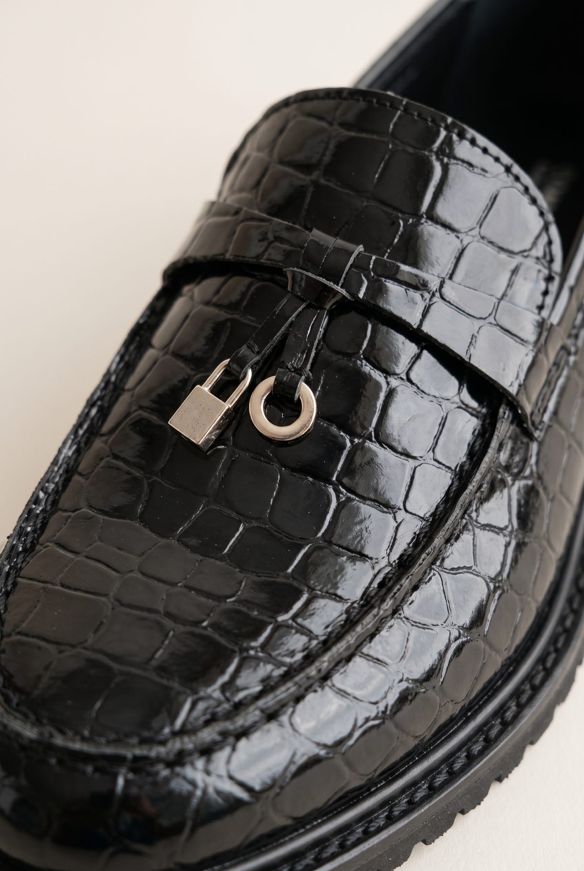 Close-up of black croc-embossed leather with a metal charm and loop on the strap and a thick lug sole edge