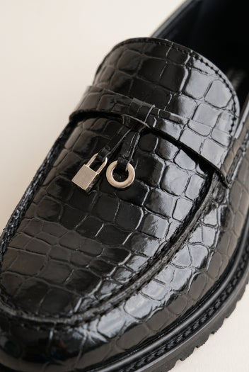 Close-up of black croc-embossed leather with a metal charm and loop on the strap and a thick lug sole edge