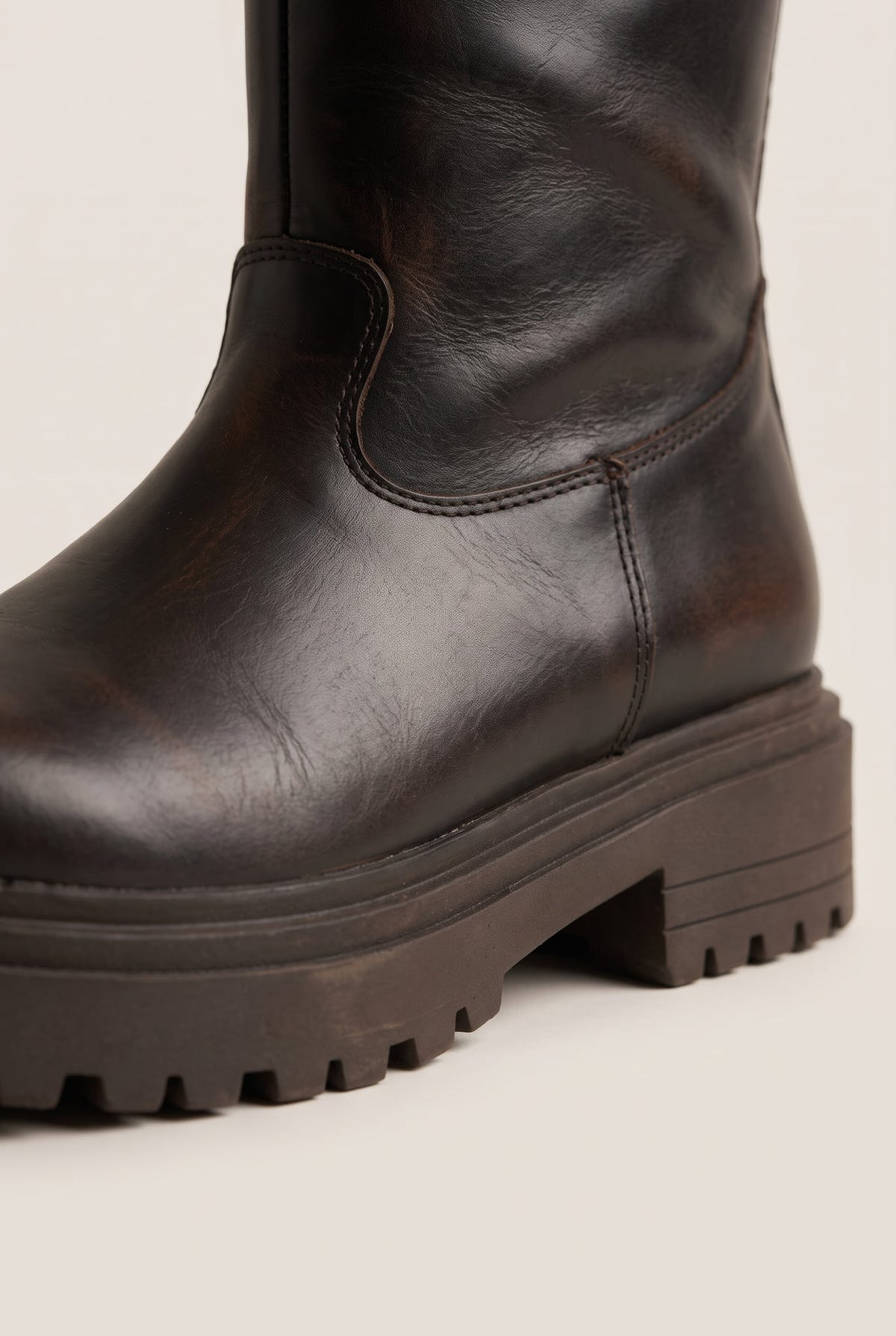 Close-up of dark brown matte boot shaft and rugged lugged sole with a rounded toe