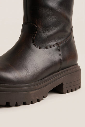 Close-up of dark brown matte boot shaft and rugged lugged sole with a rounded toe