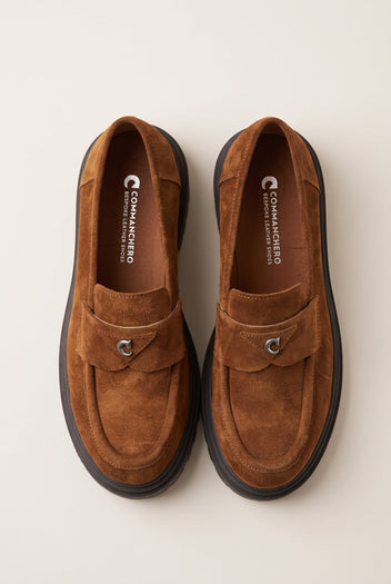 Top view of tan suede loafers with stitched strap, metal ring accent and dark chunky soles