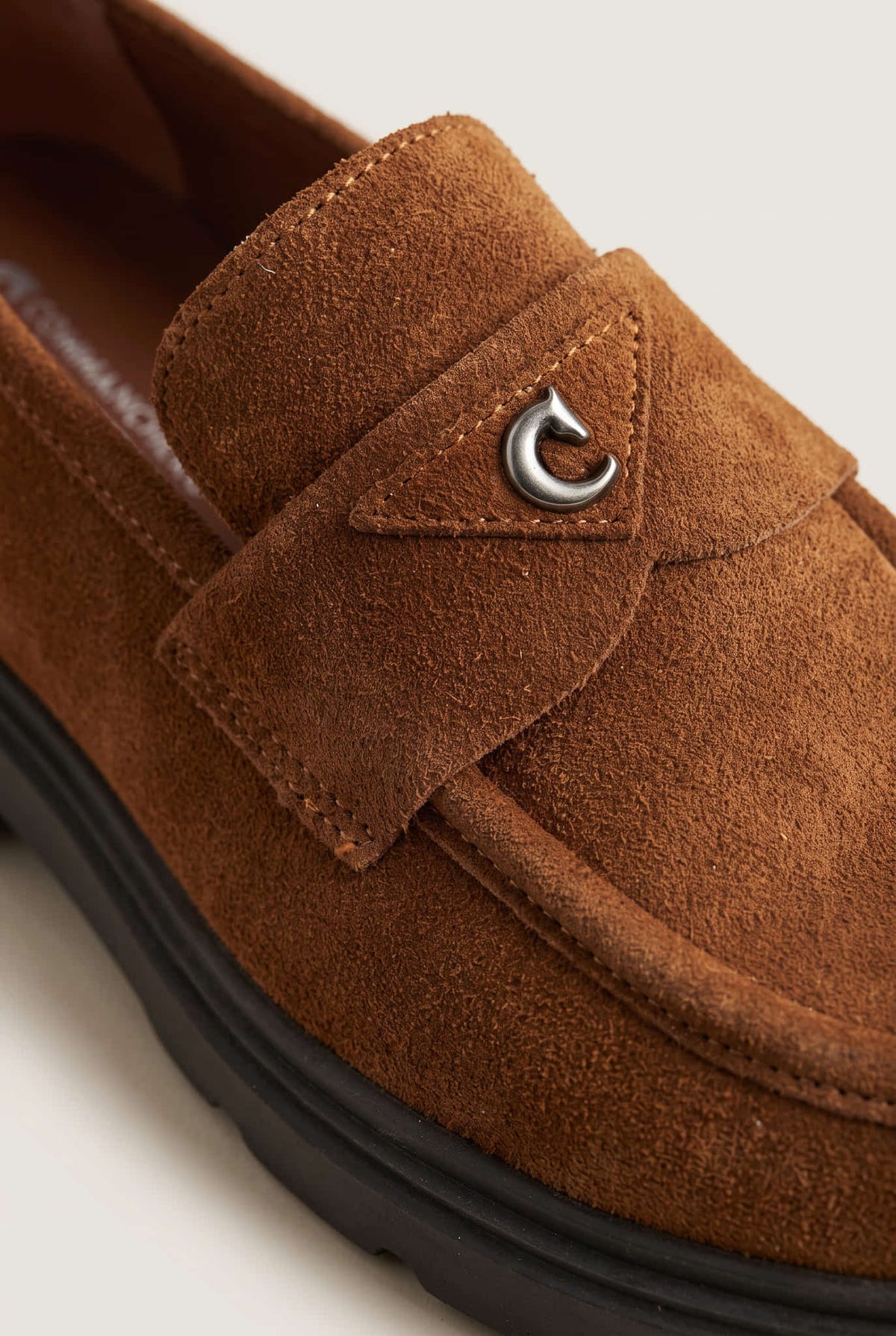 Close-up of tan suede loafer strap with stitching, metal ring accent and dark sole edge