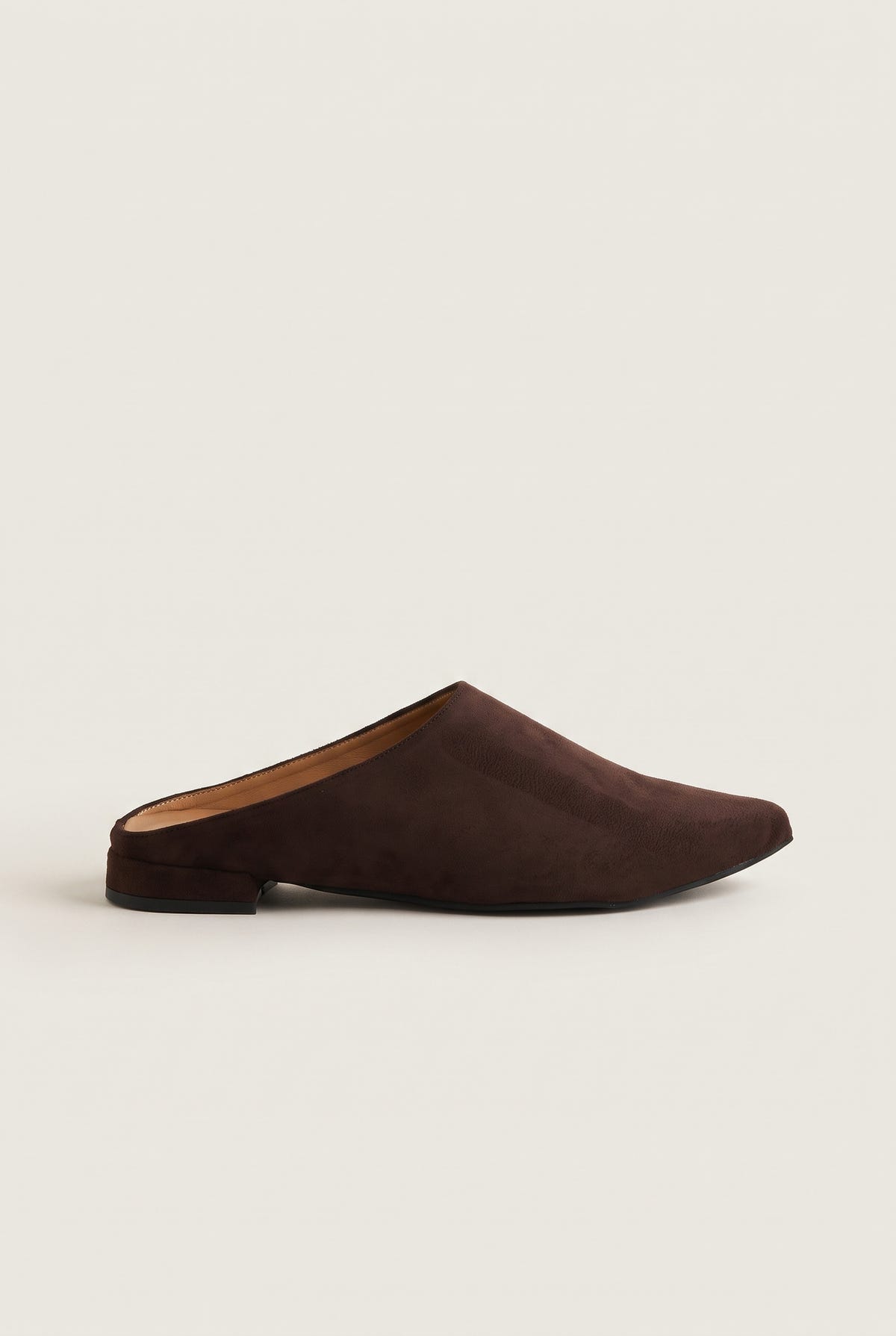 Side view of a single brown suede pointed toe mule with a low flat heel and dark sole