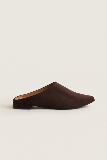 Side view of a single brown suede pointed toe mule with a low flat heel and dark sole