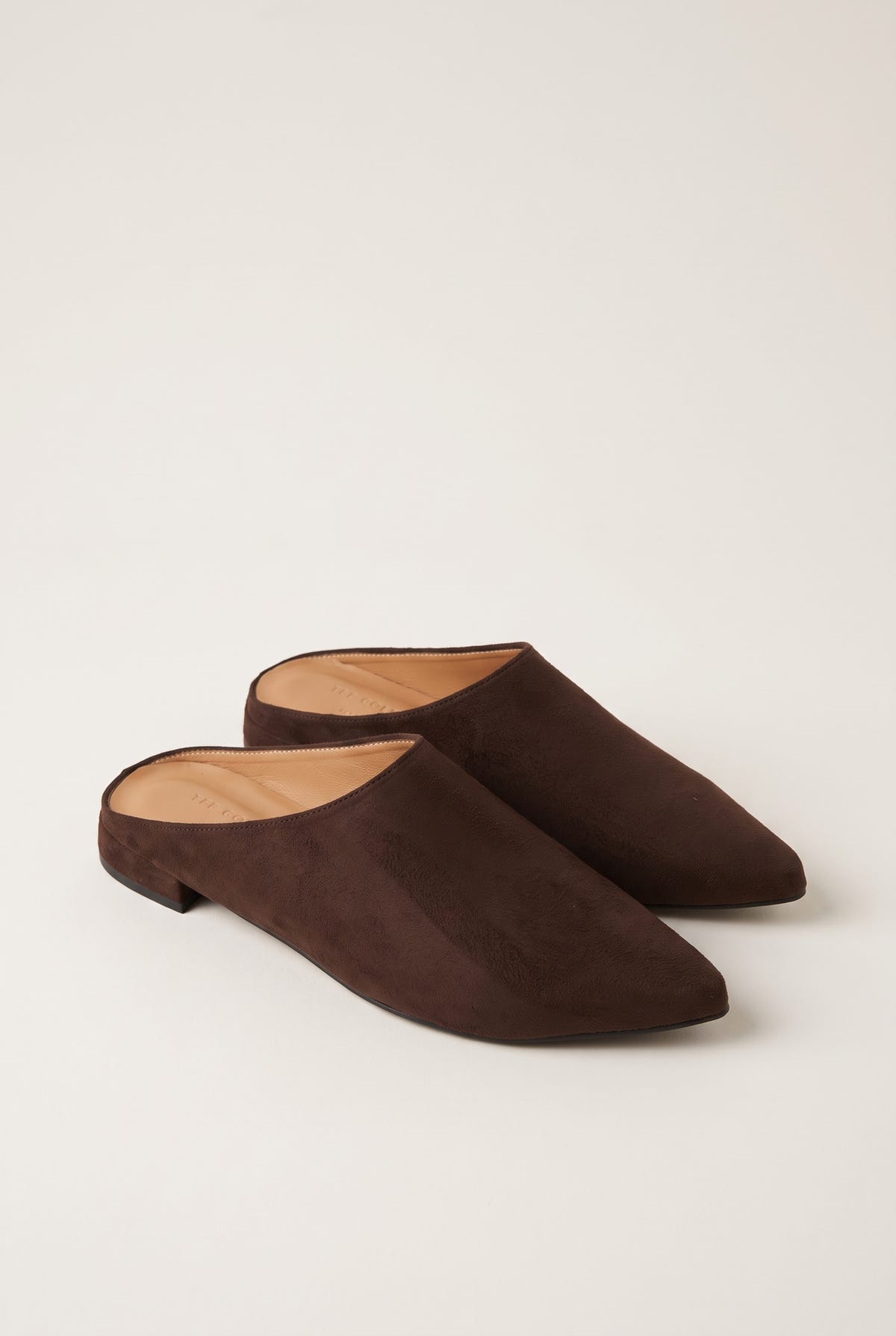 Angled view of a pair of brown suede pointed toe mules with open backs and a low flat heel