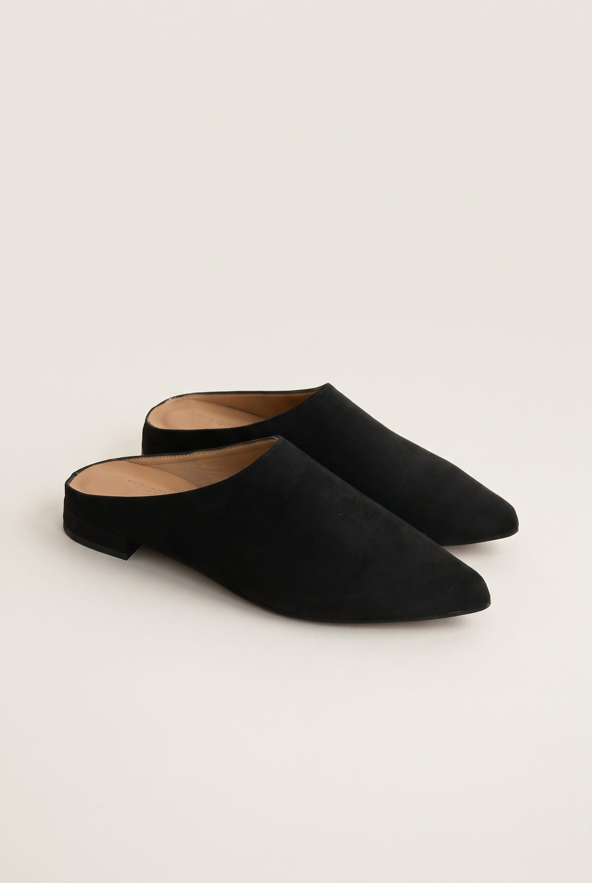 Angled view of a pair of black suede pointed toe mules with open backs and a low flat heel