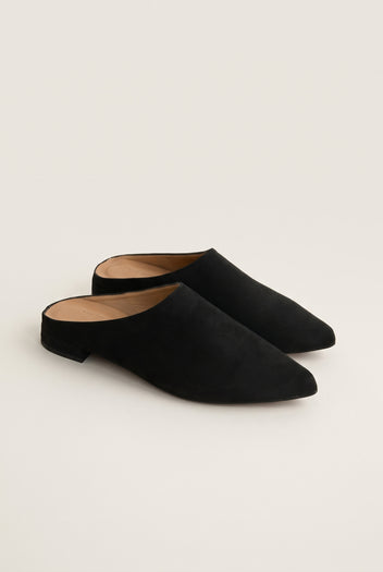 Angled view of a pair of black suede pointed toe mules with open backs and a low flat heel