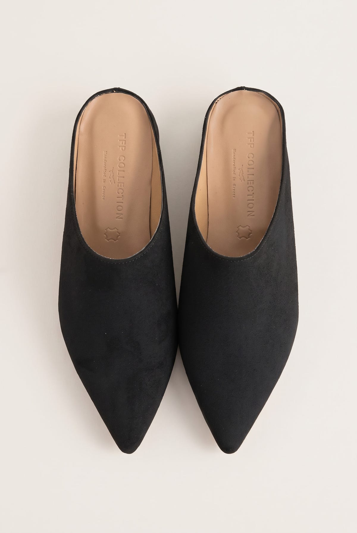 Top view of a pair of black suede pointed toe mules showing tan leather insoles and open backs