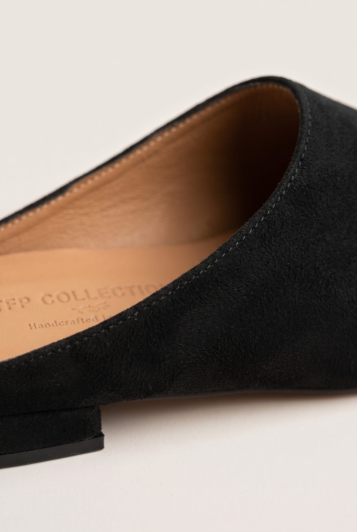 Close-up of a black suede pointed toe mule showing the tan leather insole and low heel edge