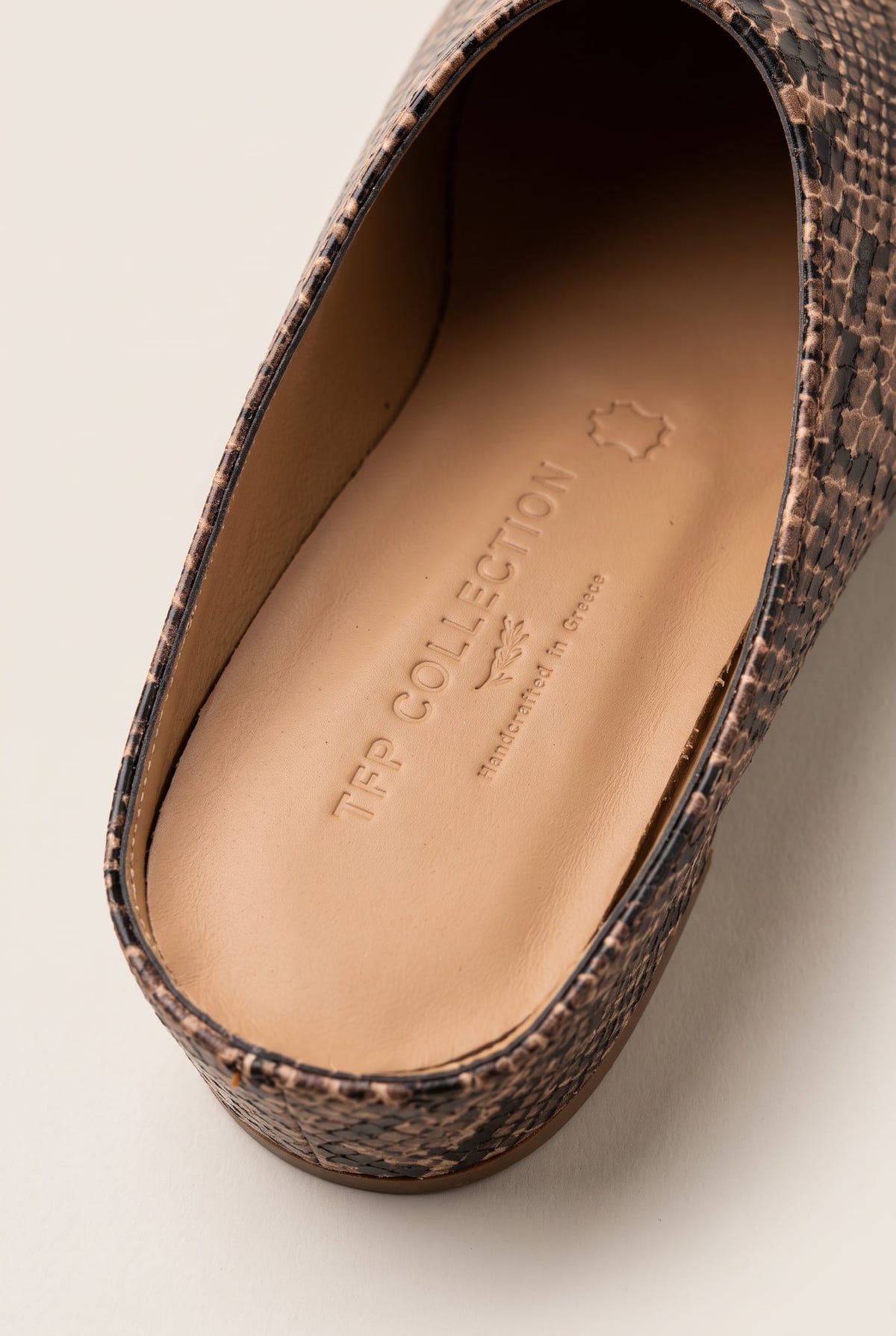 Close-up of a brown snake-effect mule showing the tan leather insole and pointed toe shape